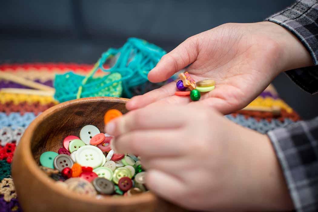 Child’s hands selecting colourful buttons from a wooden bowl.