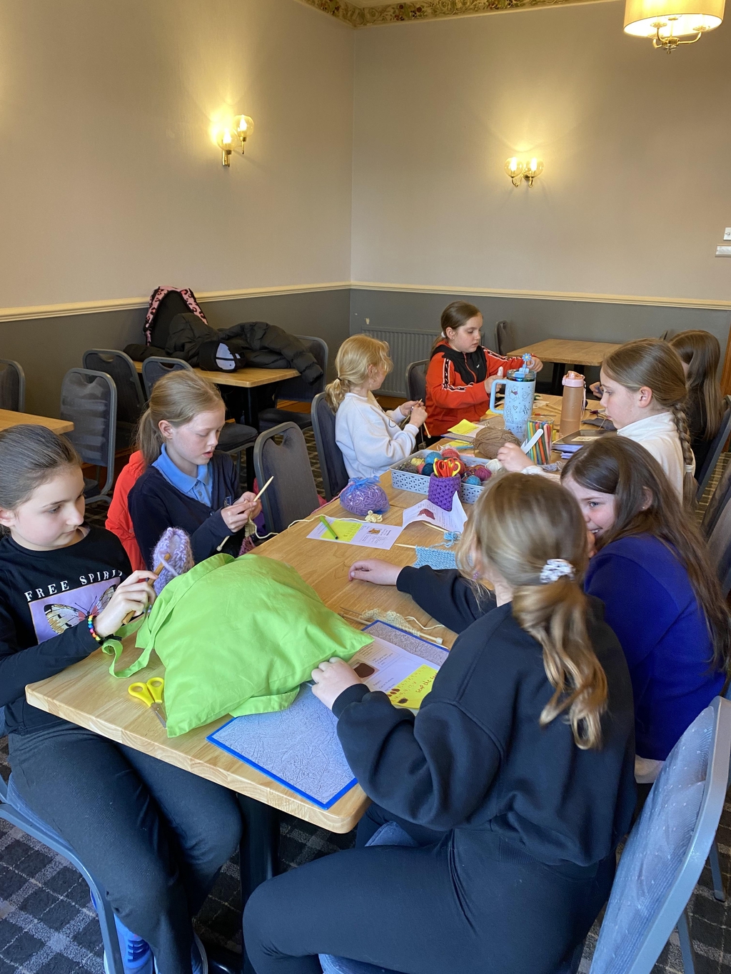 Children sitting round a table knitting and crocheting.