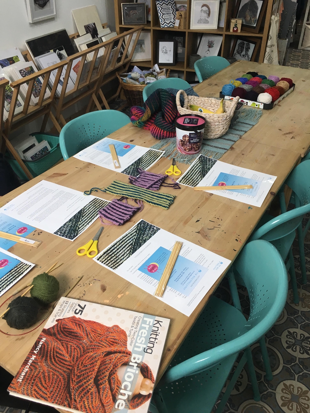 Table set up for a knitting workshop with yarn, needles, and patterns.