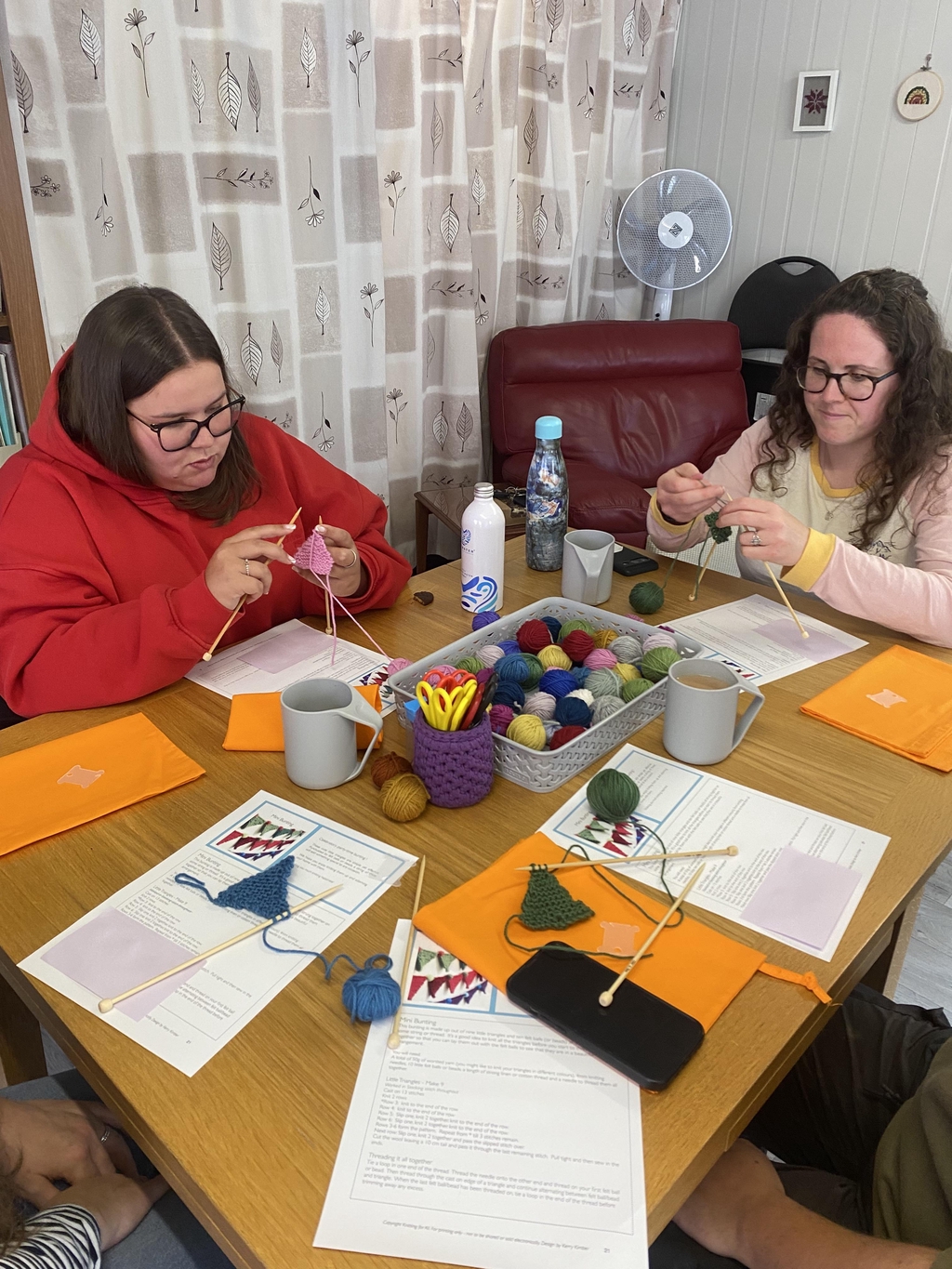 Adults learning to knit around a table with colourful yarn in the centre.