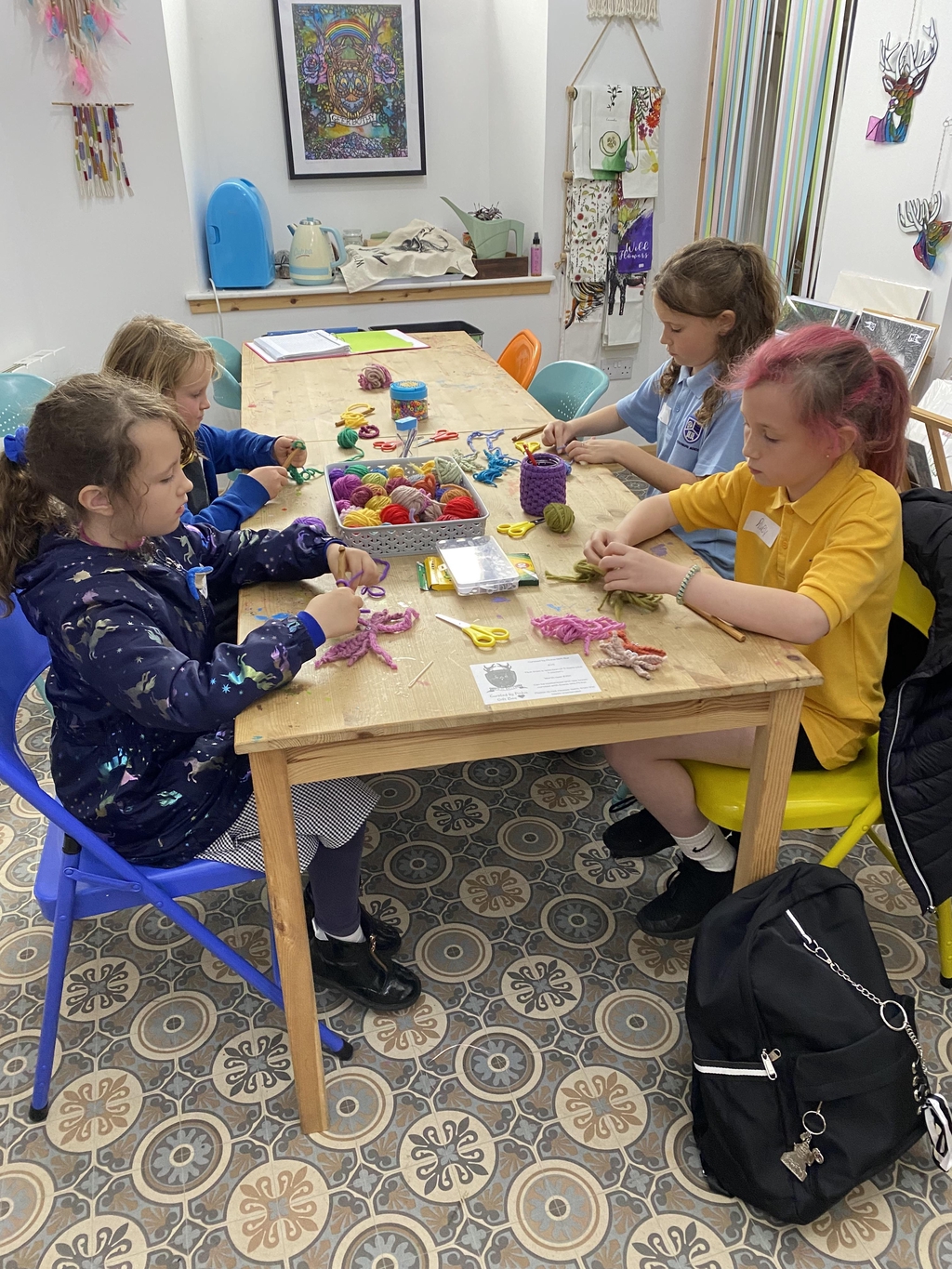 Children, at a table with colourful balls of yarn in a basket. learning to crochet.