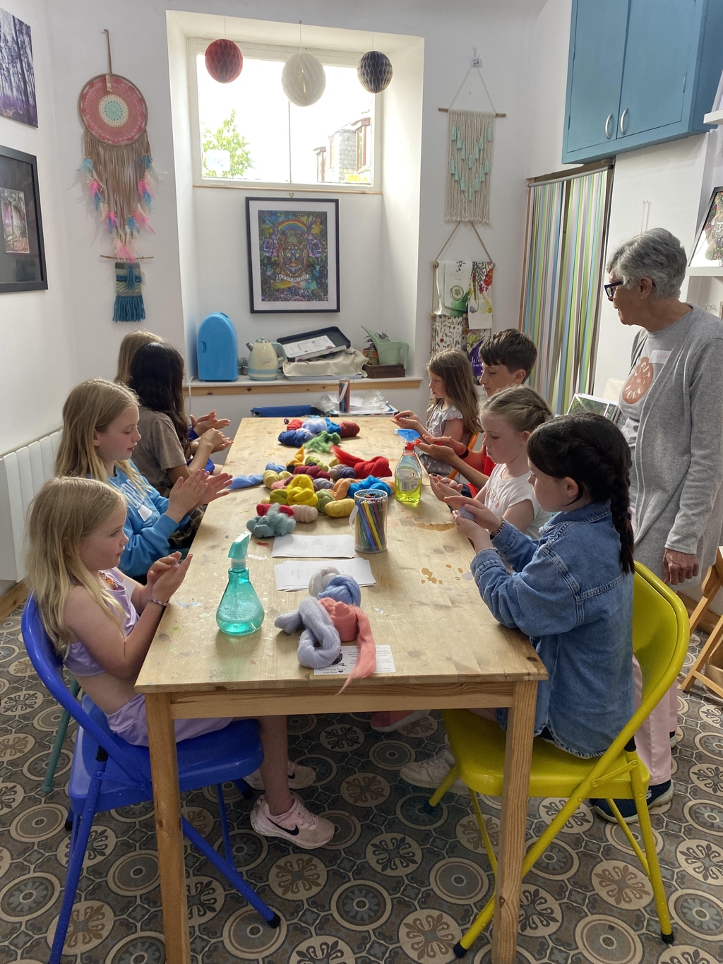 Children, at a table with colourful balls of roving learning to make wet felted ball toppers for their own knitting needles.