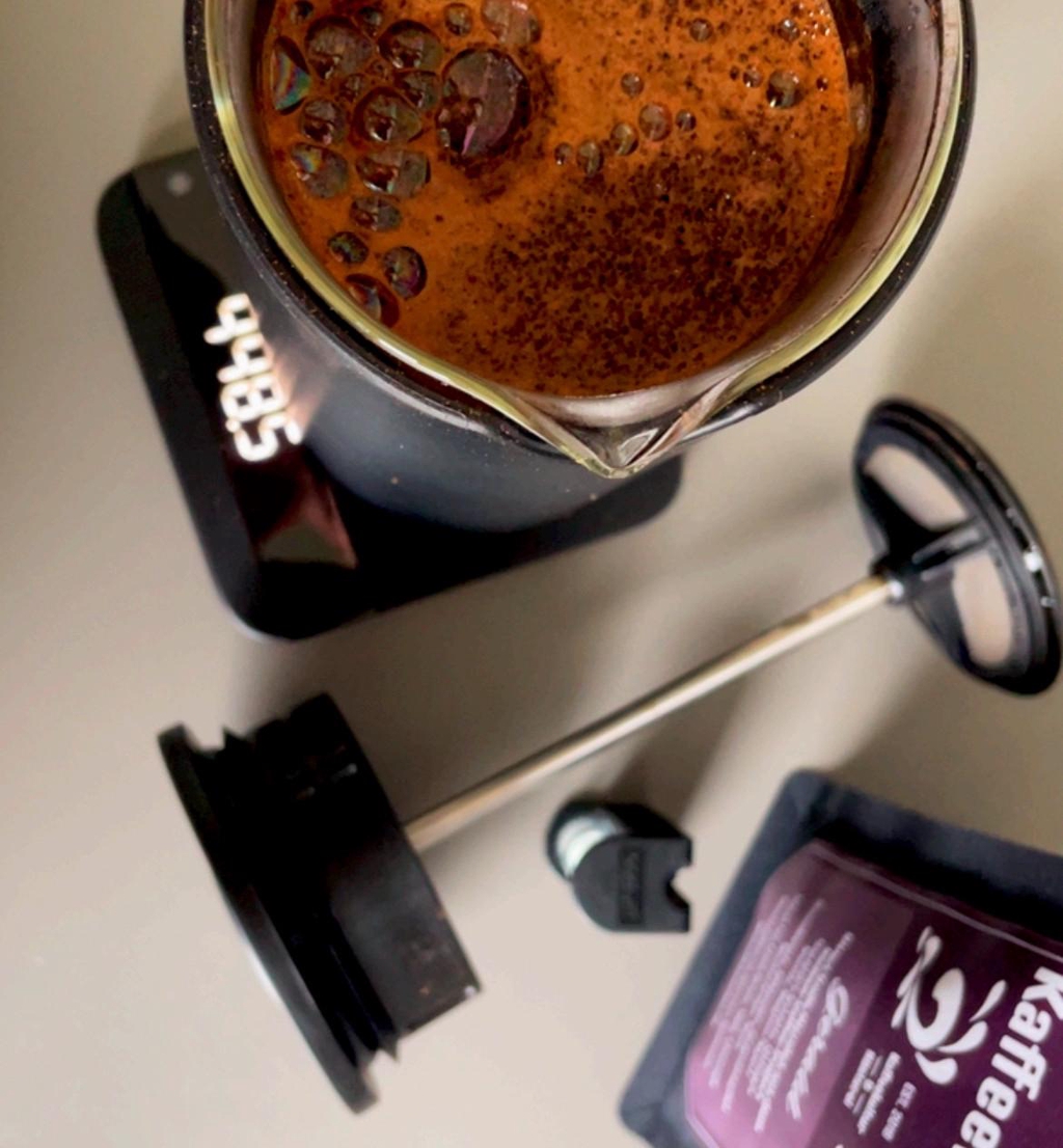 Das Bild zeigt die Zubereitung mit der Stempelkanne (auch French Press, Bodum, Drückkanne genannt). Der Kaffee ist gerade frisch aufgegossen und zeigt ein schönes Blooming.