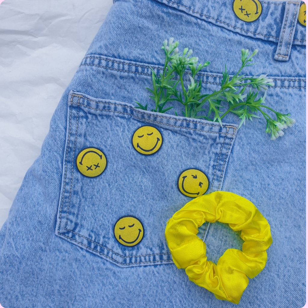 Yellow scrunchie against denim trousers with yellow smiley face patches and plants