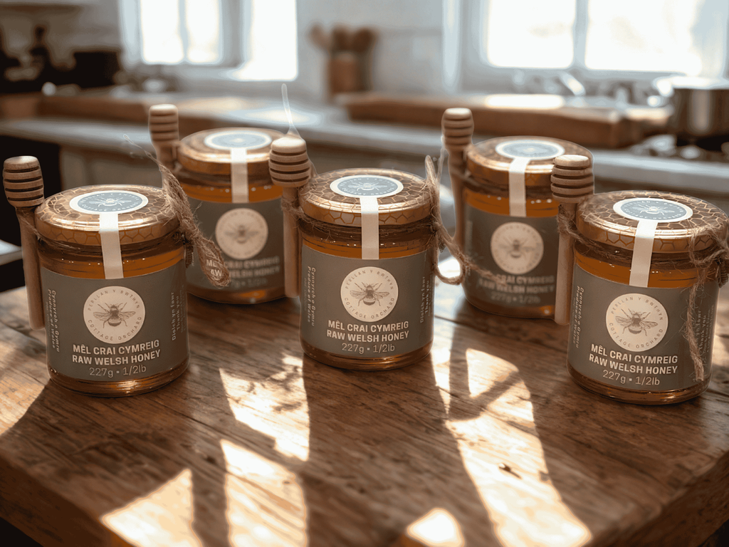 Jars of golden Cottage Orchard honey on a wooden table. Jariau o fêl aur Cottage Orchard ar fwrdd pren.