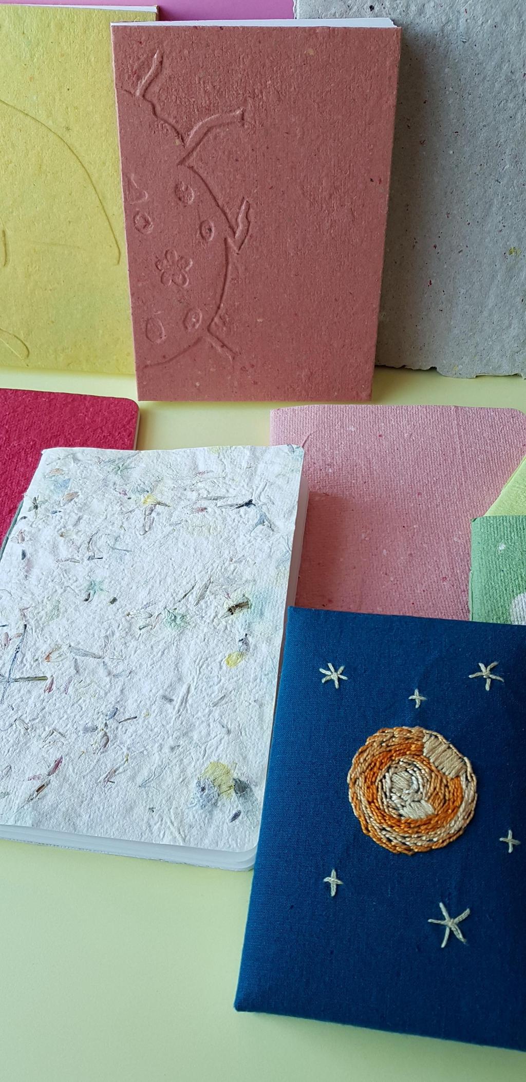 Carnet divers disposé sur un fond uni. Carnet avec inclusion végétale, carnet brodé, et en papier recyclé