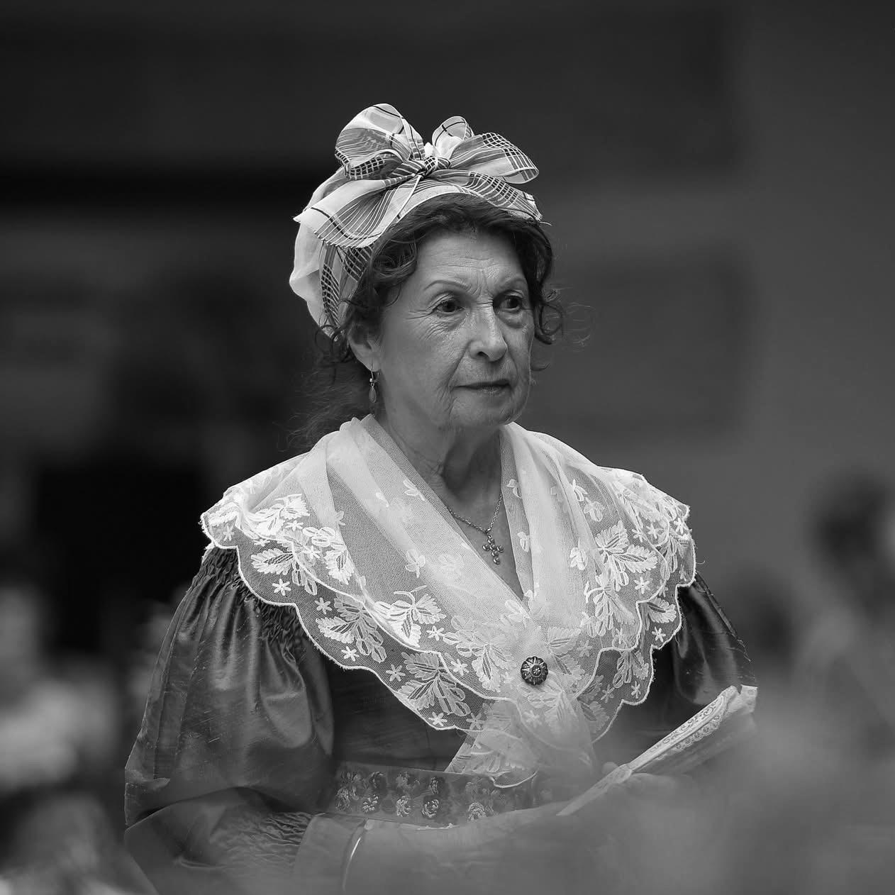 Portrait en noir et blanc d'une femme vêtue d'un costume traditionnel provençal, le costume d'arlésienne, avec une coiffe élégante et des détails en dentelle. Cette image met en lumière le riche héritage culturel de la Provence, un mélange d'authenticité et d'élégance intemporelle qui inspire les créations modernes de Vestimentari.