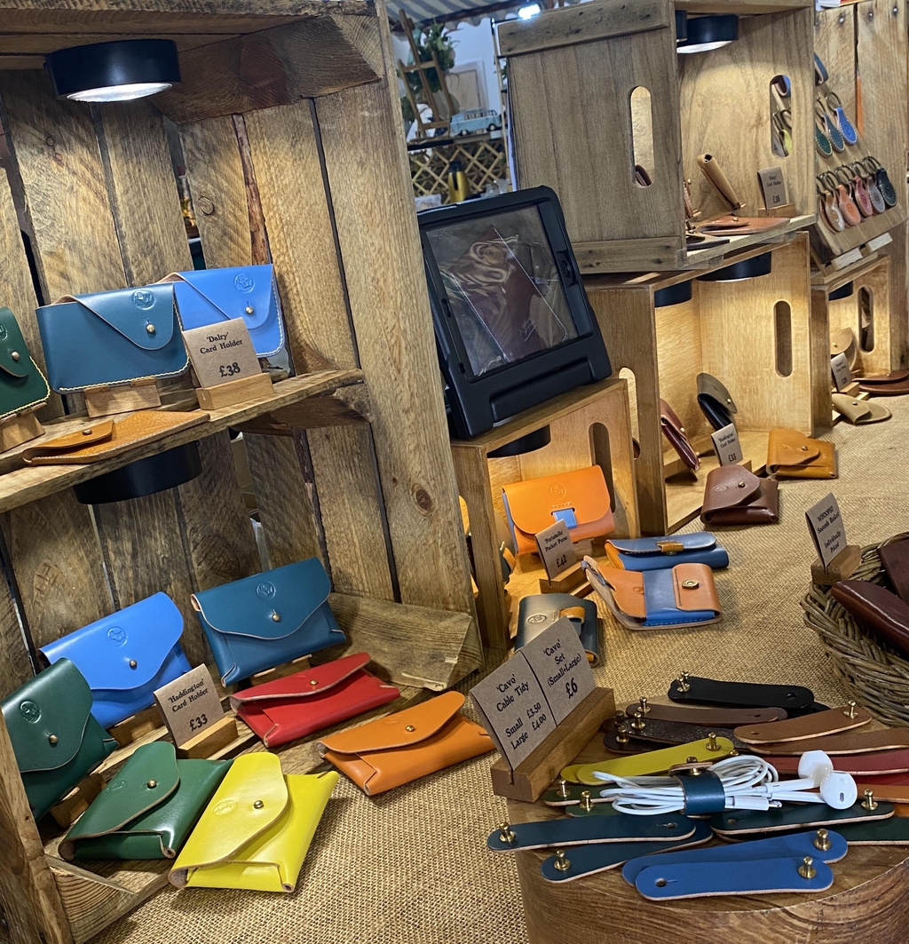 Photo showing the range of Broken Wing Leathercraft Studio card holders displayed in down lit wooden crates with the Headline "This Little Piggy Went  to Market..." and "We're super chuffed to be trading at the Makers Market - Archerfield Walled Garden, North Berwick on Saturday 26th September  11am-4pm!"