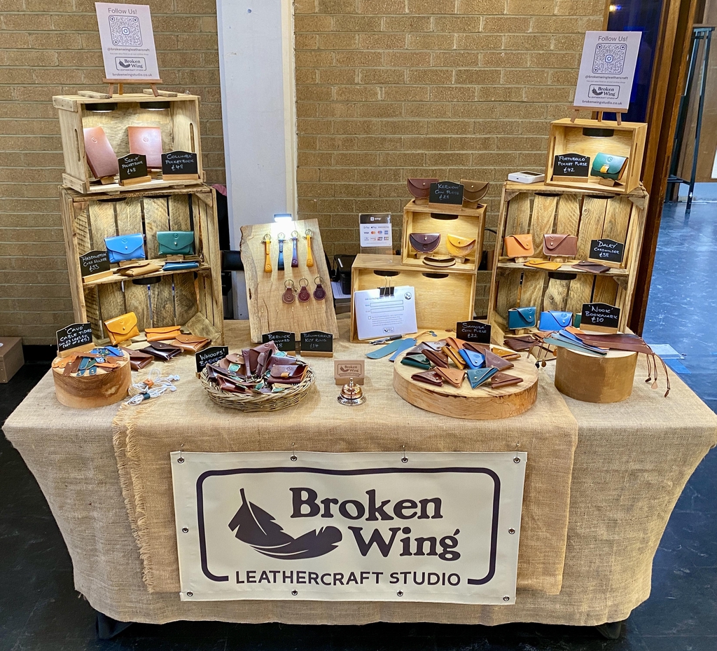 Photo showing the range of Broken Wing Leathercraft Studio card holders displayed in down lit wooden crates with the Headline "This Little Piggy Went  to Market..." and "We're very excited to be trading at Linlithgow Night Market on Friday 28th August!"
