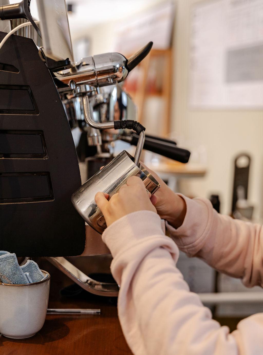 Barista preparing coffee with a portafilter and milk jug on a professional espresso machine at Castle Street Coffee.