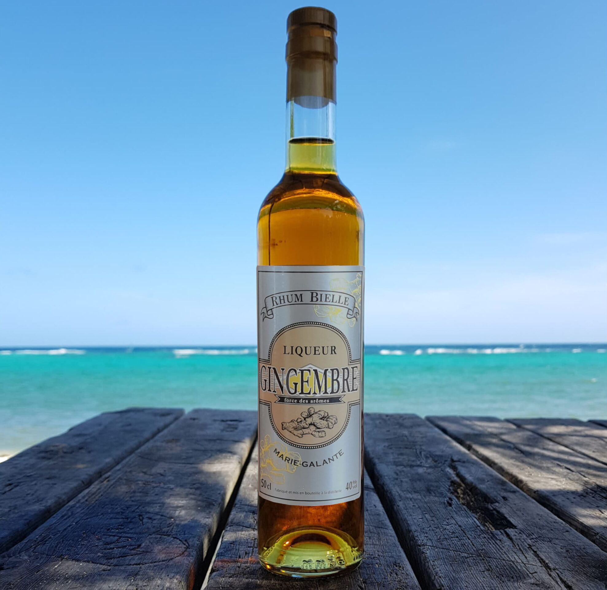 Bouteille de liqueur de rhum au gingembre L'Atelier du 7 posée sur une table face à la mer