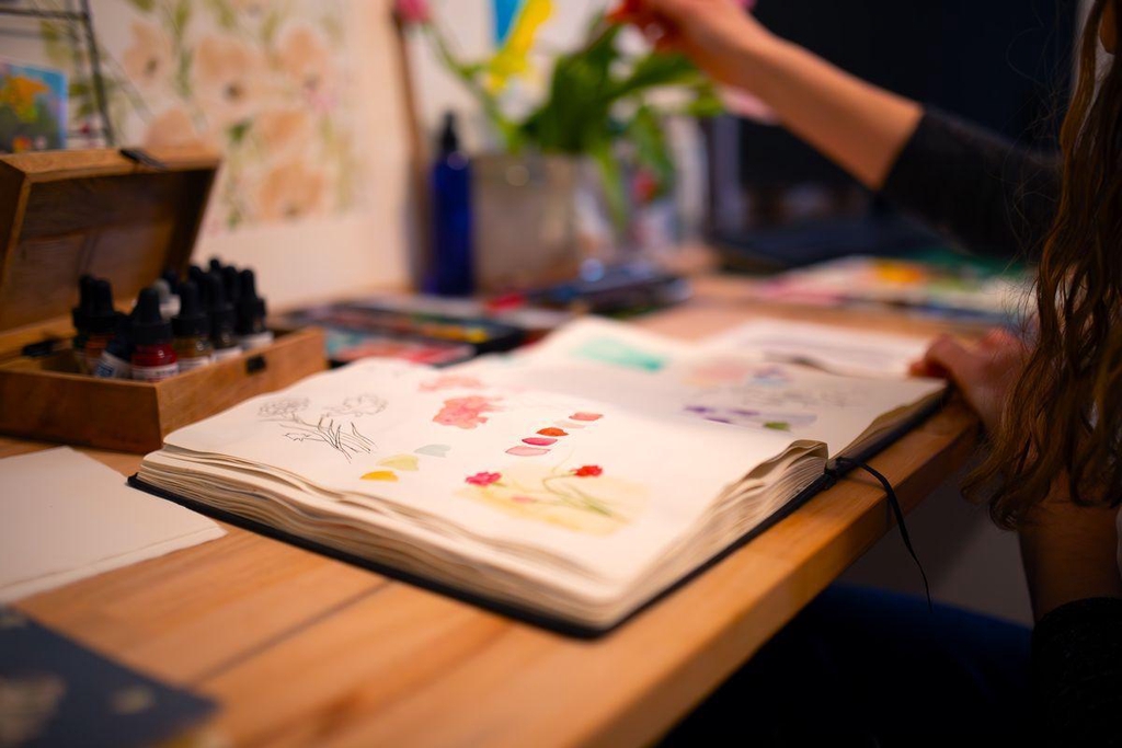 Vue en gros plan du sketchbook de Sybile Coré ouvert avec des dessins et des essais de palette de couleurs sur son bureau dans son atelier d'artiste.