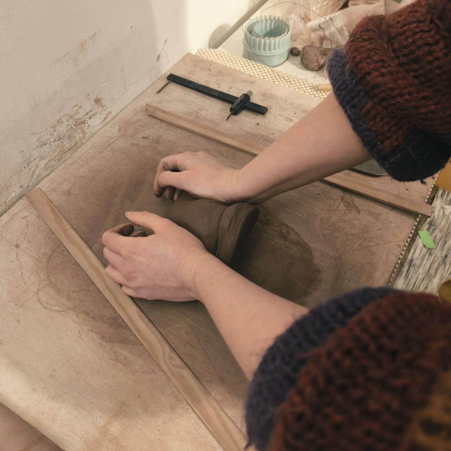 L'artisane céramiste en plein travail de création dans son atelier, travaillant la terre brute à la main.