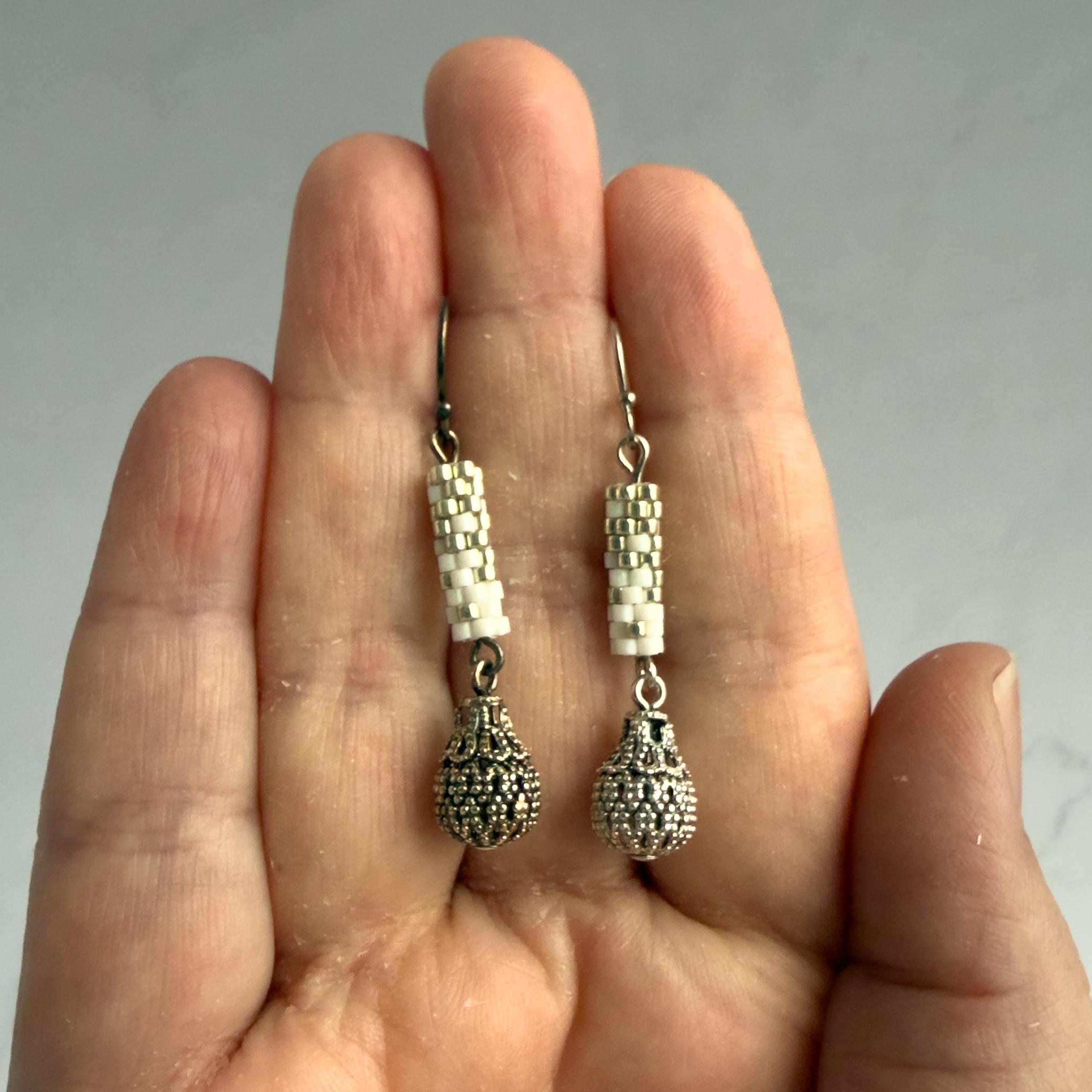 Résultat du nettoyage au bicarbonate de soude sur des boucles d'oreilles en perles tissées blanches : boucle de gauche encore oxydée, boucle de droite retrouvant son éclat après nettoyage