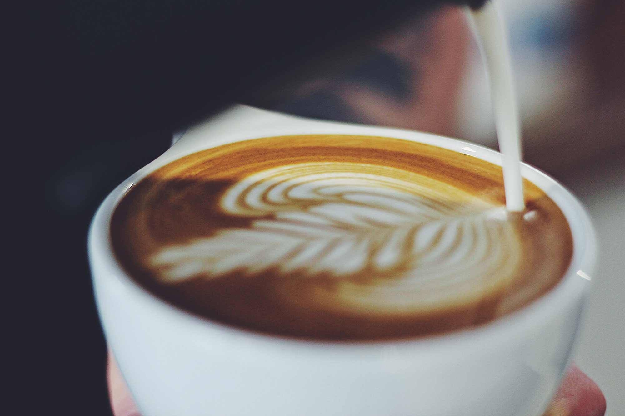 Picture of a cup of coffee with latte art being poured