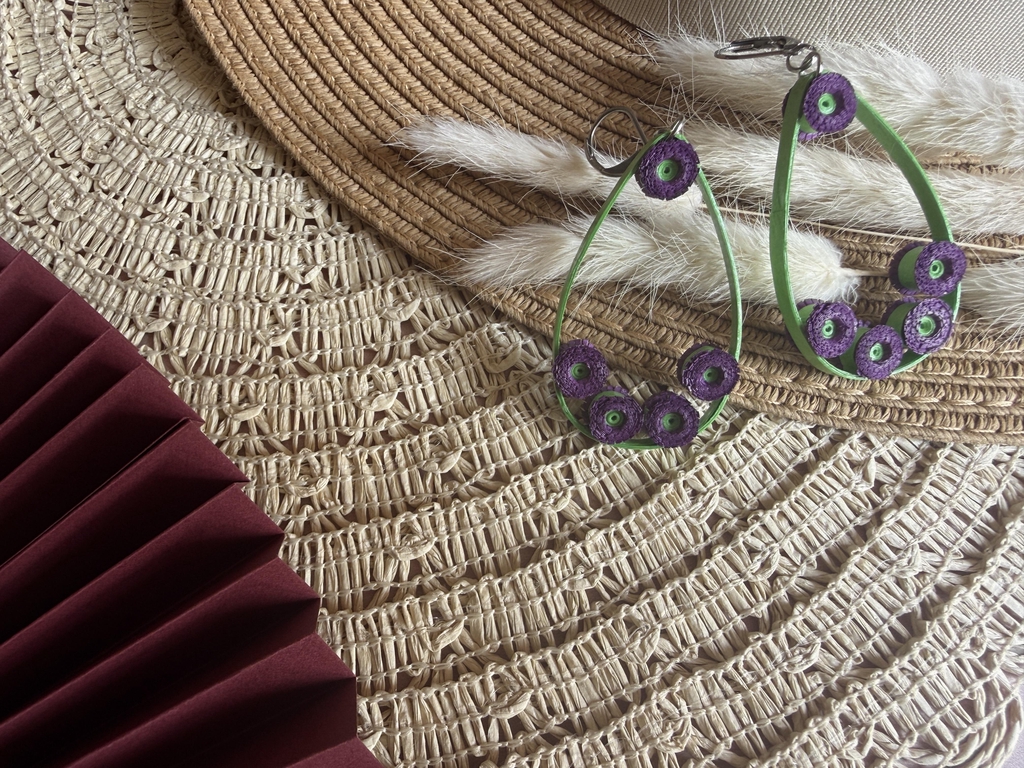 Paire de boucles d'oreilles pendantes en papier avec monture en forme de goutte verte . De petites pâquerettes violettes à cœur vert sont disposées sur la monture. Fermoirs dormeuses (argentés).