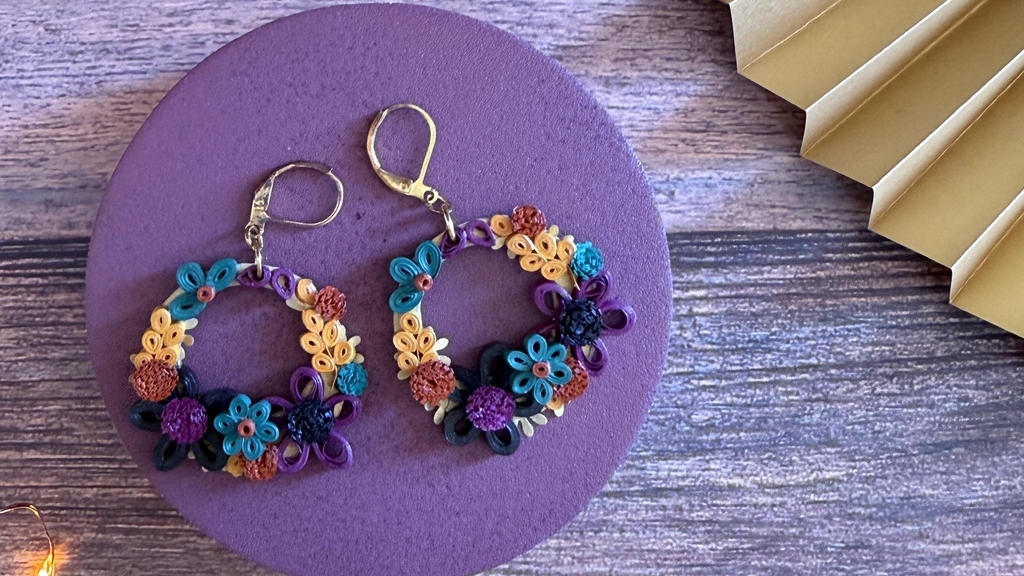 Paire de boucles d'oreilles pendantes en papier avec monture en forme de goutte bleu . De petites pâquerettes fuchsia  à cœur bleu sont disposées sur la monture. Fermoirs dormeuses (argentés).
