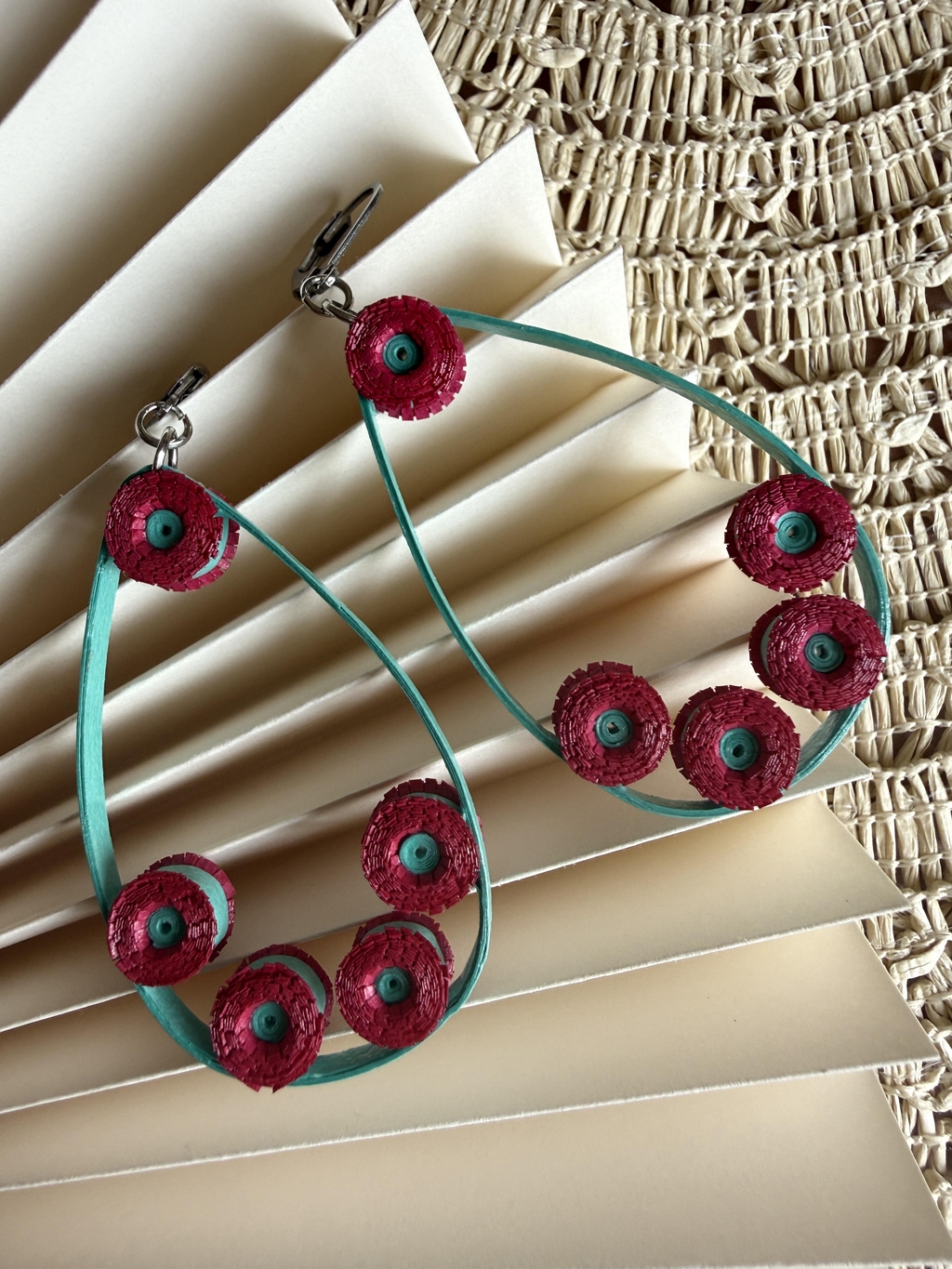 Paire de boucles d'oreilles pendantes en papier avec monture en forme de goutte bleue . De petites pâquerettes fuchsia à cœur bleu sont disposées sur la monture. Fermoirs dormeuses (argentés).