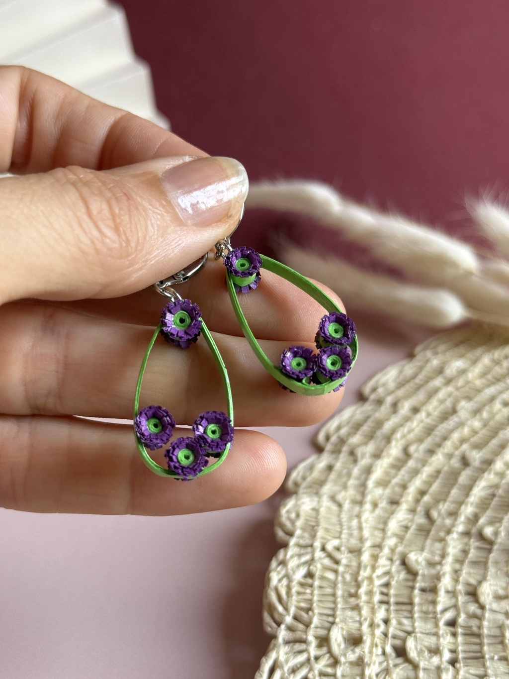 Paire de boucles d'oreilles pendantes en papier avec monture en forme de goutte verte . De petites pâquerettes violettes à cœur vert sont disposées sur la monture. Fermoirs dormeuses (argentés).