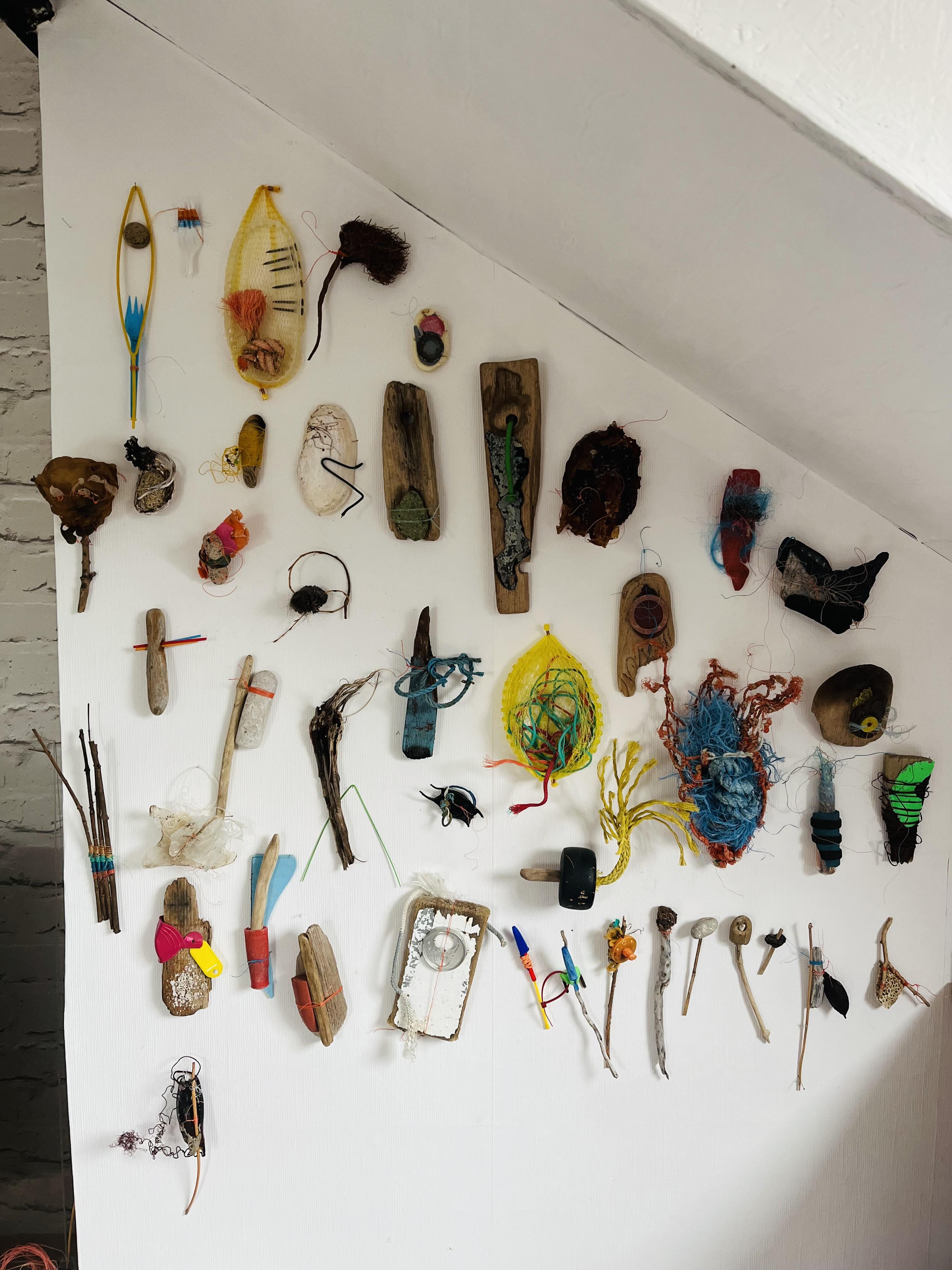 Jane Wood | contemporary sculpture and assemblage  | The image shows a white wall with a range of small objects displayed that are made from found objects and materials.