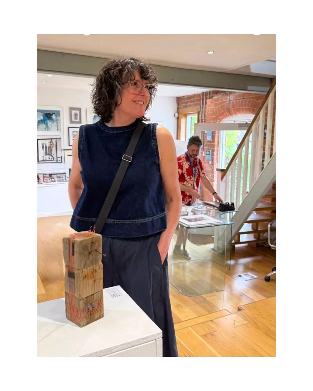 A woman standing infront of a wooden sculpture in a gallery
