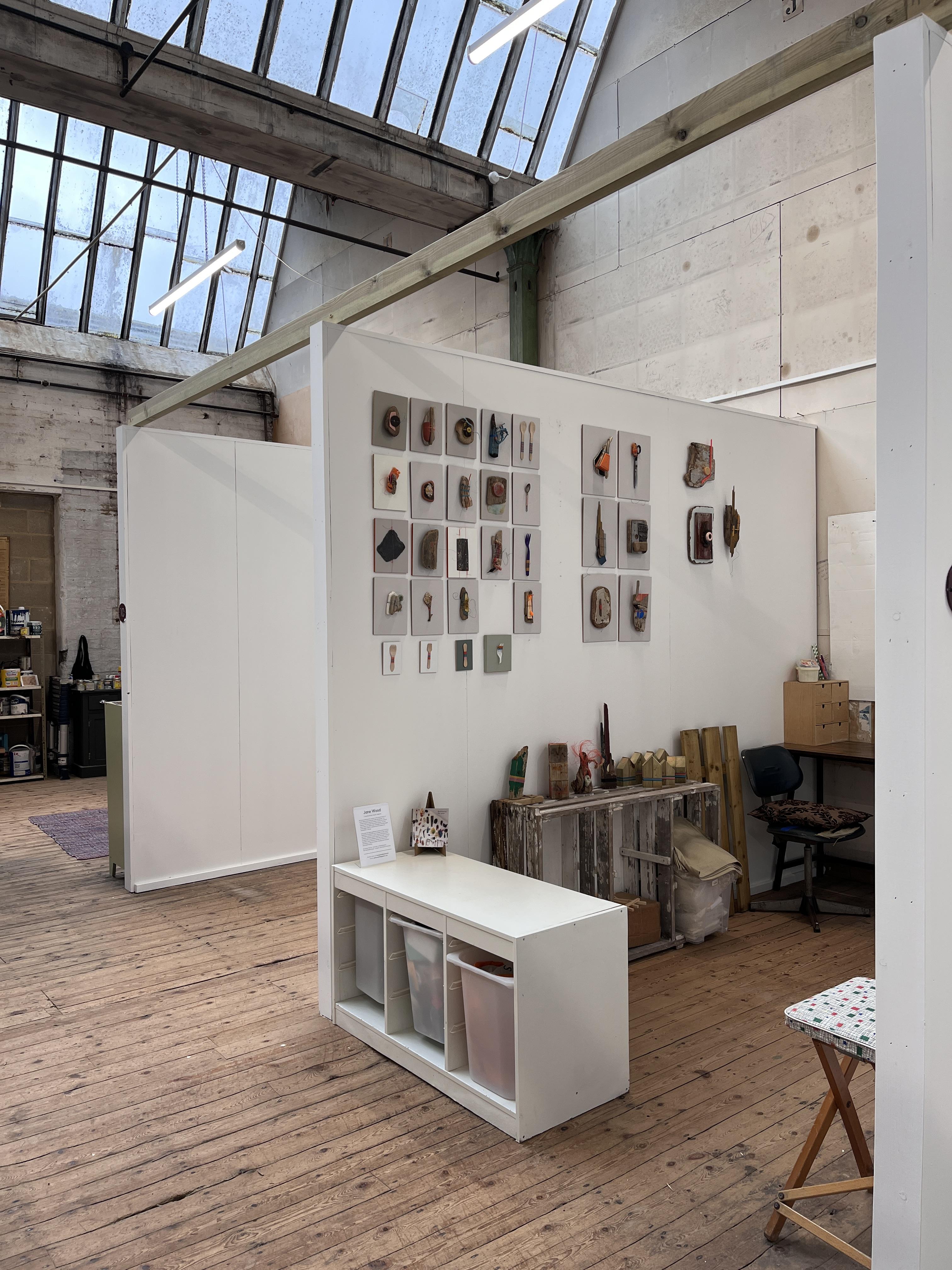 3D Wabi-sabi wall art, assemblage and sculpture.
The image shows the corner of a large mill room at Sunny Bank Mills with a glass ceiling and bare wood floors. There is an art studio space that shows 3D wall art - sculpture and assemblage made form found objects displayed on the wall.
