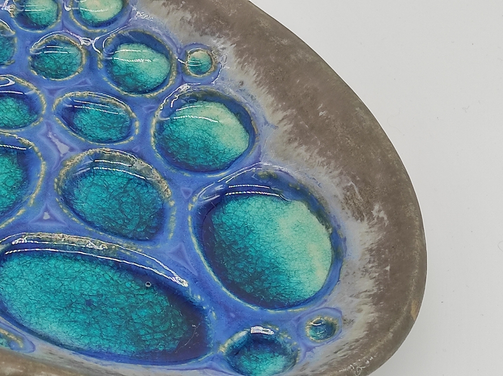 Detalhe de travessa de cerâmica artesanal com esmalte azul turquesa brilhante e textura de círculos cavados à mão.