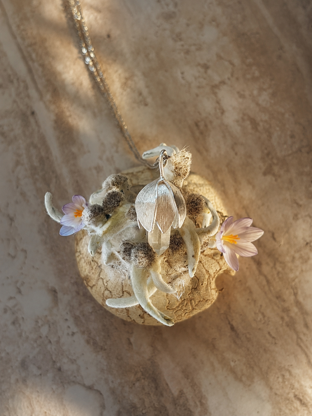 Photo d’un pendentif en argent, fabriqué à la main dans mon atelier, qui représente un crocus de montagne avec une pointe de quartz de Savoie
