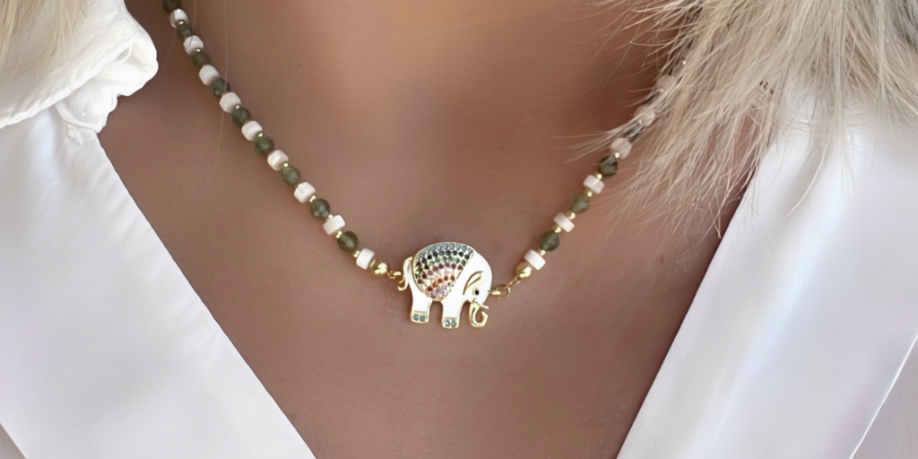 Femme portant un collier artisanal Sandja Créations composé de perles en apatite verte, blanches (Nacre), dorées (plaqué or 18 carats) et d’un pendentif éléphant émaillé blanc avec des zircons colorés, bijou fait main et élégant