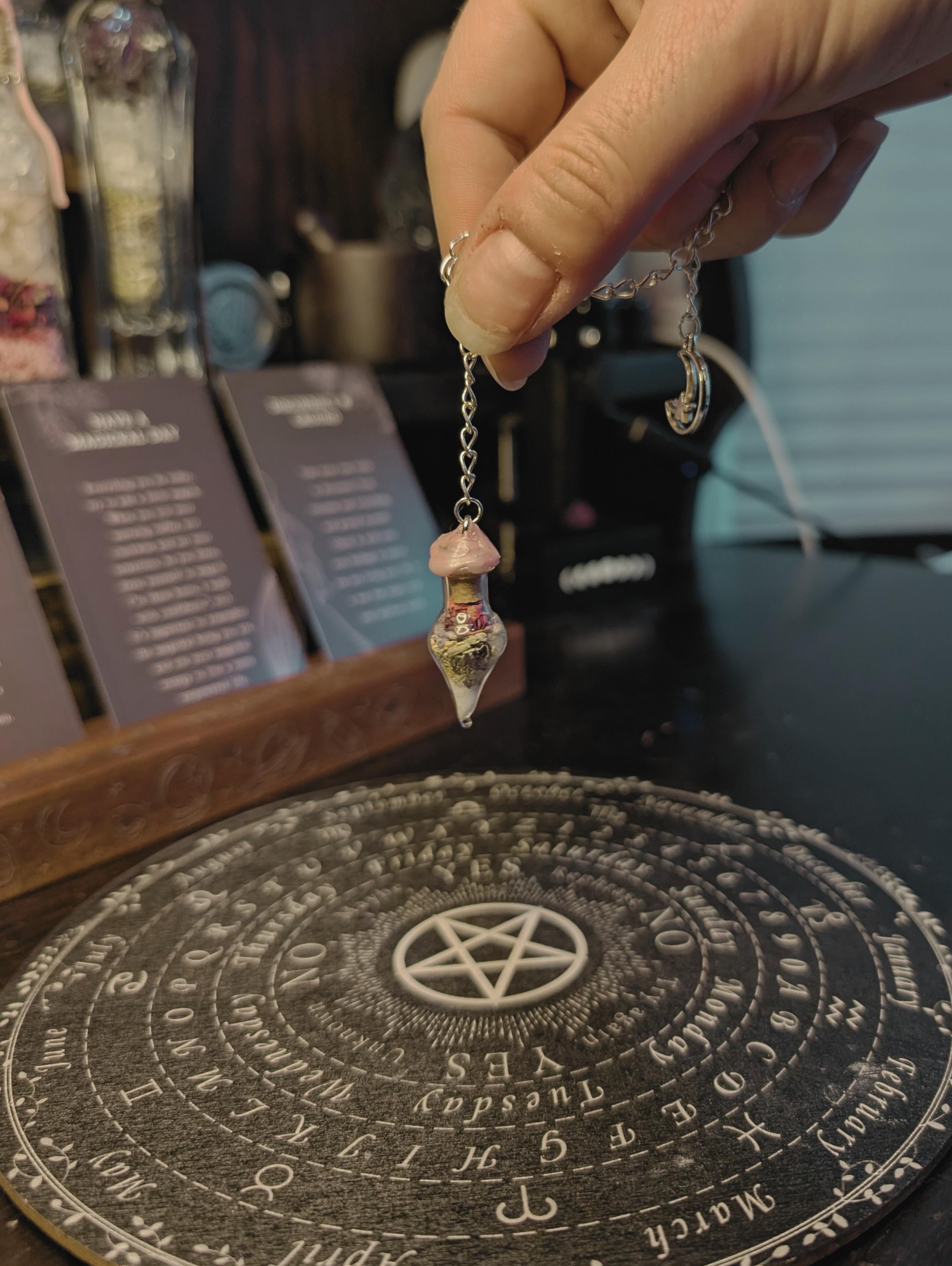A dowsing pendulum being held over a pendulum board to divine answers from the higher self
