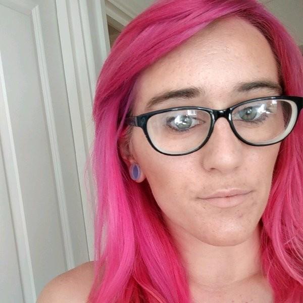 A photo of Danielle, the maker behind Starrmie's Sanctum. The photo shows a girl with vibrant pink hair and black thick rimmed glasses