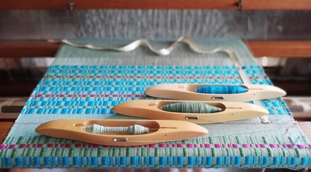 photographies Atelier Tisse Natura tissu en coton lin en cours de tissage sur métier à tisser, navettes de tissage et bobines de fil