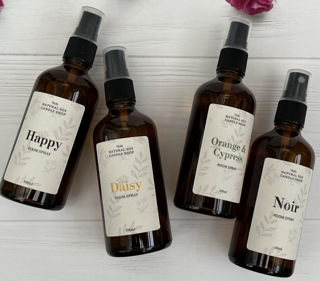 Four amber glass spray bottles filled with fragrance, they have natural soy candle shop on the labels.