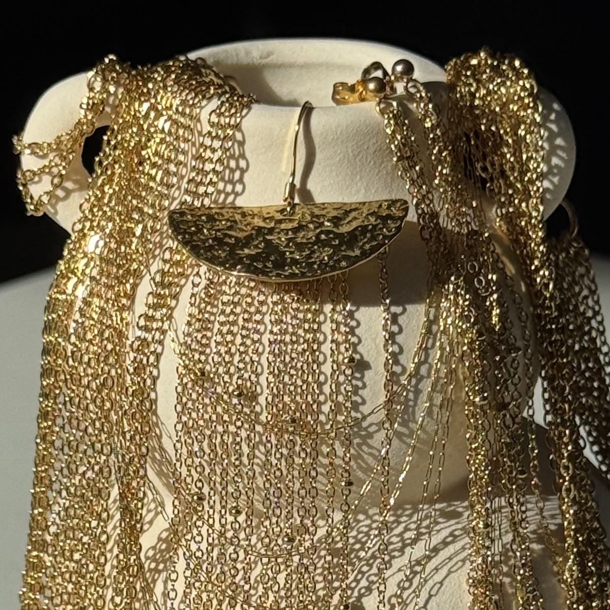 Bijoux dorés en acier inoxydable présentés sur vase blanc avec accumulation de chaînes fines qui brillent.