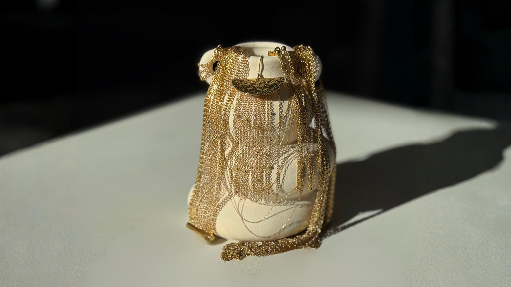 Bijoux Harmonie Joyae en acier inoxydable doré sur un vase blanc, bagues, boucles d'oreille, bracelets et colliers fins avec chaînes accumulées, faits main en édition limitée pour femme.