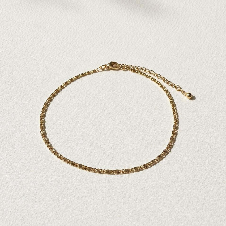 Bracelet de cheville doré en acier inoxydable présenté seul, avec une chaîne fine et des motifs inspirés des coquillages.