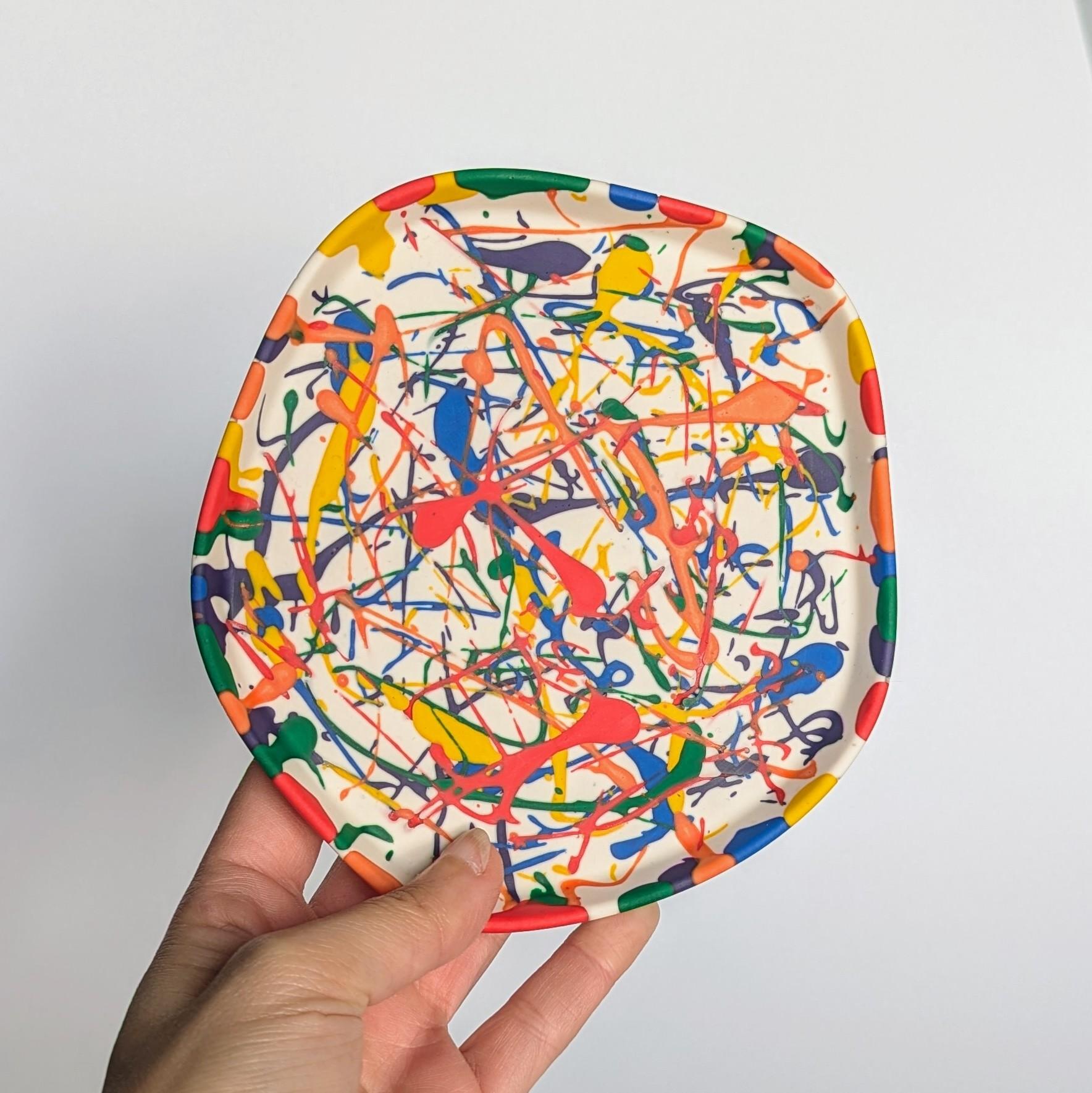 Colourful organically shaped tray with a rainbow splatter design on a white background