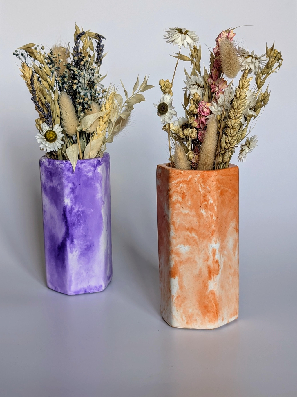 Two colourful vases holding dried flowers, one is purple and the other is orange