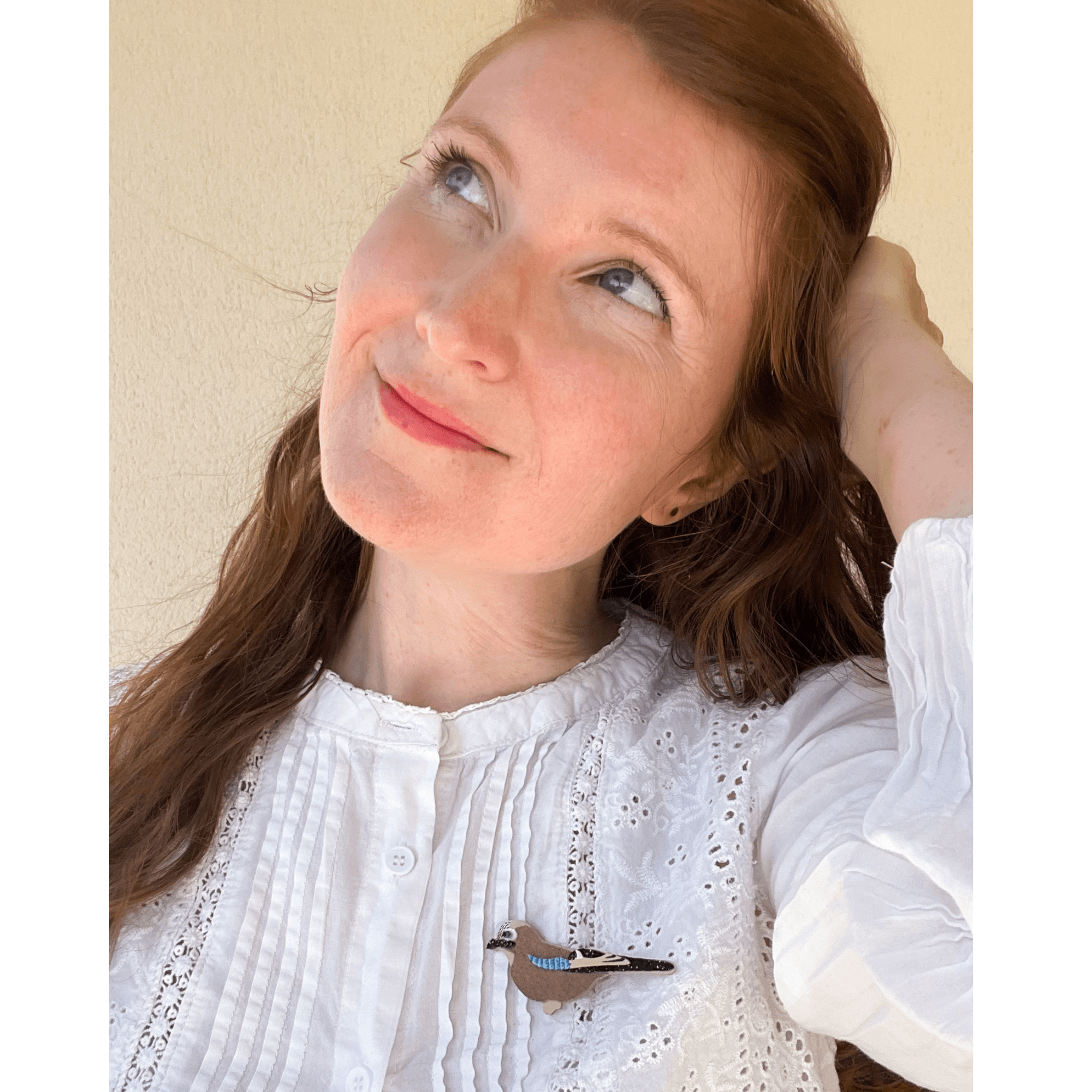 Amandine Quinton, la créatrice des bijoux Le nid de la mésange, portant des boucles d'oreille paon fait main en broderie or.