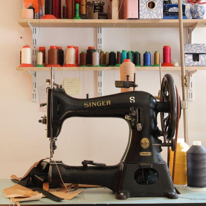 Machine à coudre Singer ancienne dans un atelier de maroquinerie avec bobines de fil colorées en arrière-plan