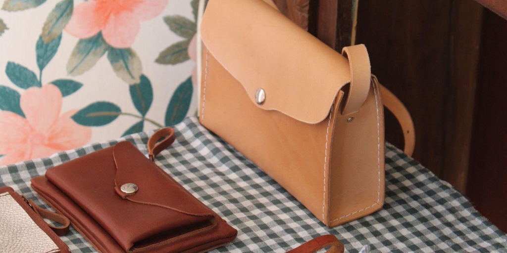 Créations en cuir 31 mai : sac, porte-cartes et bracelets exposés sur une table à motif vichy dans un décor chaleureux. Image illustrant les points de vente de la marque.