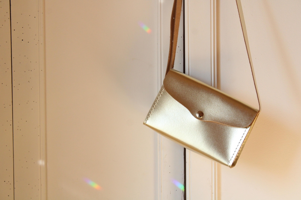 Pochette dorée à bandoulière suspendue à une porte, photographiée dans une lumière douce. Image d’ambiance pour annoncer la présence de 31 mai aux marchés de Noël.