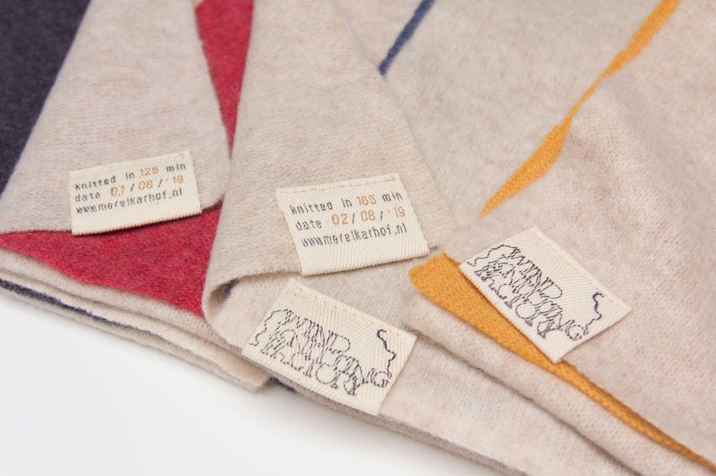 Close up image of the labels which every wind knitted scarf gets. When the knitwear gets ‘harvested’ and transformed into scarves they are labelled with the time and day the wind created the sustainable fashion scarf. 