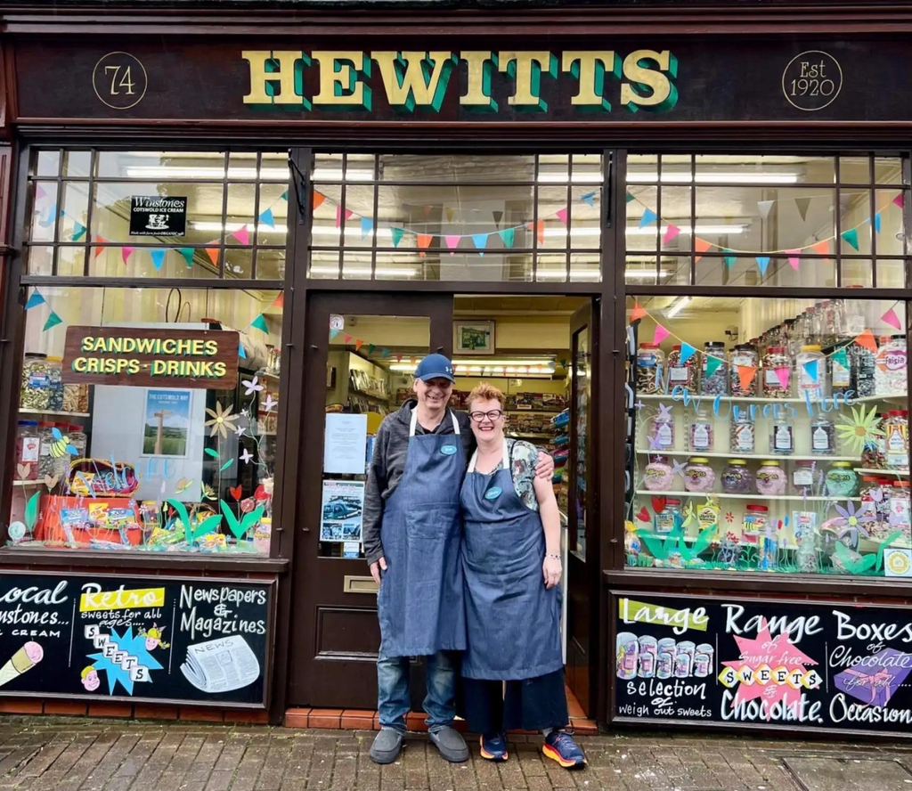 The exterior of Hewitts sweet shop, with owners Claire and Jim Parry standing in front smiling widely.