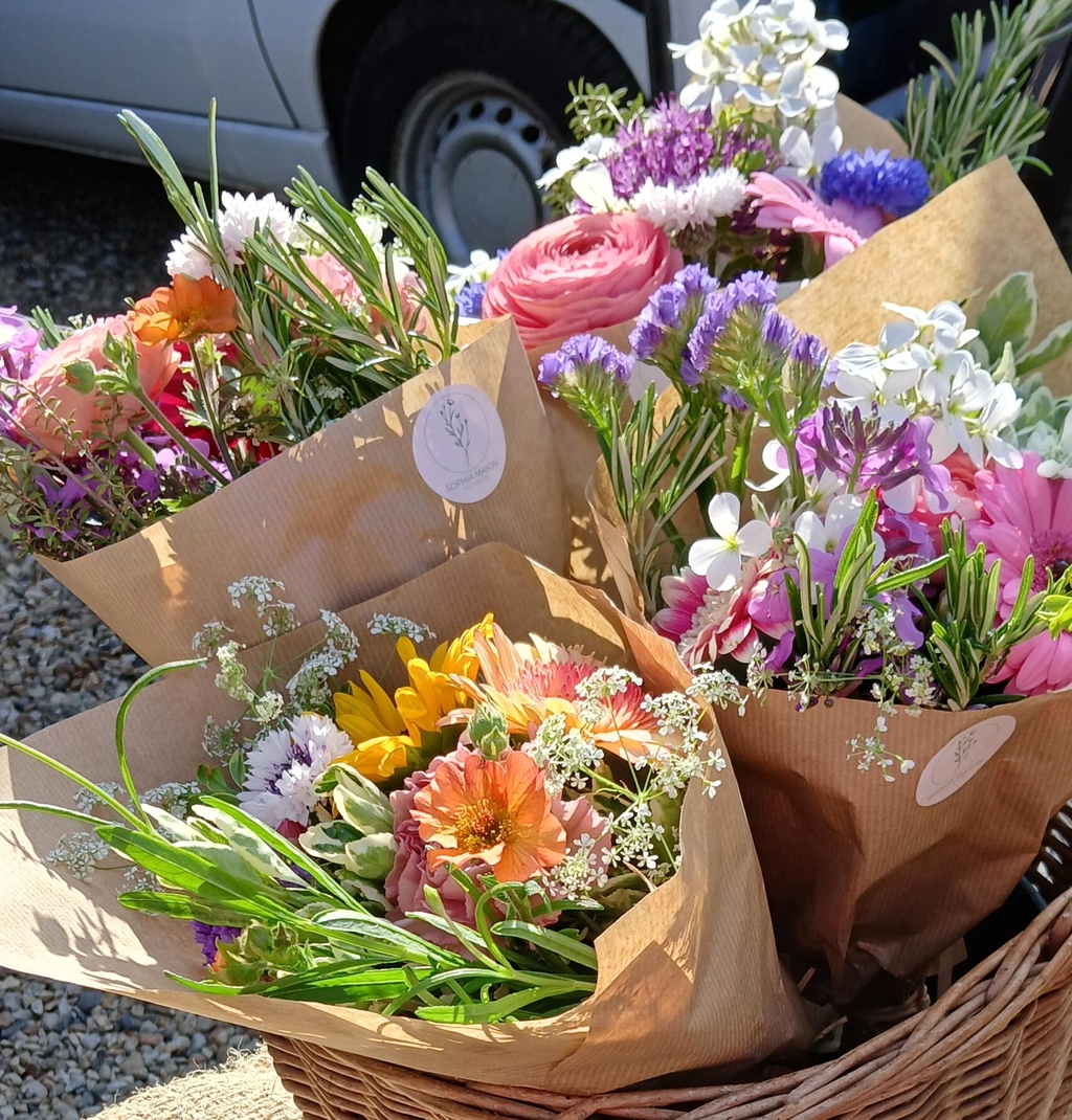 Several small bouquets of colourful spring flowers, wrapped in paper and displayed for sale in a basket.