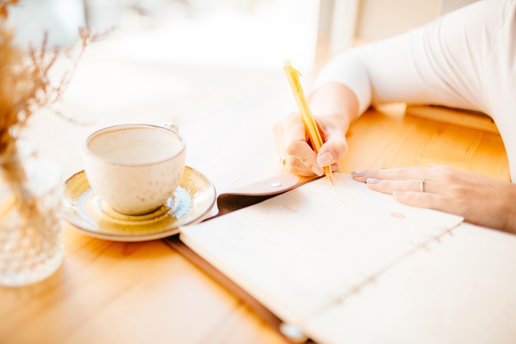 Autorin Lena Österle, wie sie im Café sitzt und schreibt. Neben ihr steht ihr Lieblingsgetränk: Kaffee.